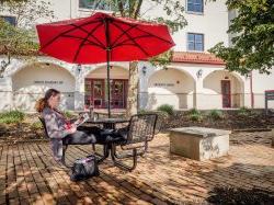 一个学生坐在护理学院和研究生院外面，在一个阳光明媚的日子里，在桌子伞下看书.