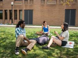Students sitting in the grass outside of Calcia Hall having a conversation.